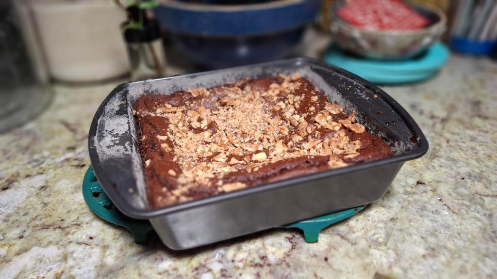 P:an of black bean brownies with walnuts on top, sitting on a counter