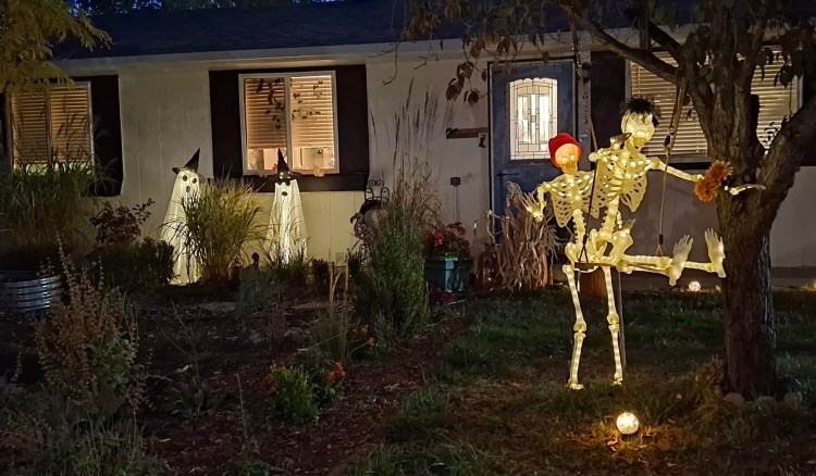 two skeletons playing on a tree swing, two ghosts standing by the house, all lit up on a dark night